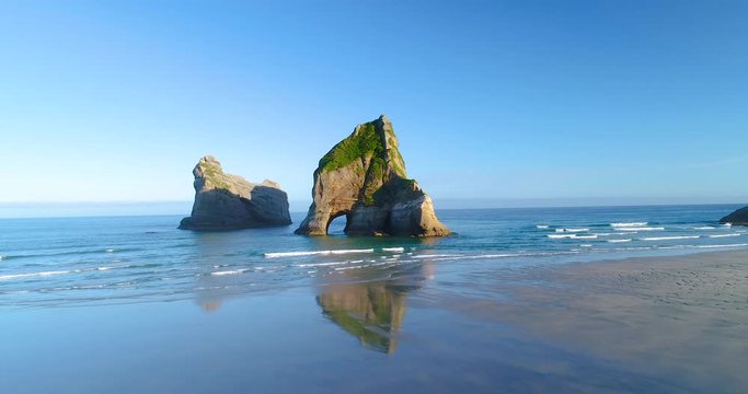 Aerial 4k forwartd tracking from low angle motion view of the rock formations of Archway Islands that sit just off shore of Wharariki Beach on the northern tip of the south island of New zealand
