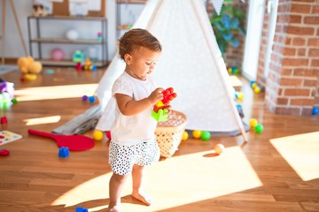 Adorable toddler playing with building blocks around lots of toys at kindergarten
