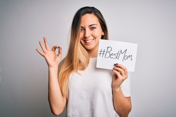 Young beautiful woman holding paper with best mom message celebrating mothers day doing ok sign with fingers, excellent symbol