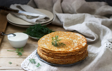 Buckwheat pancakes served with sour cream and dill on a wooden table. Rustic style.