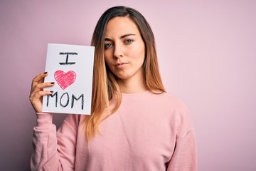 Young beautiful woman holding paper with love mom message celebrating mothers day with a confident expression on smart face thinking serious