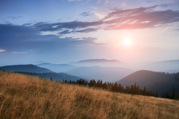 Fototapeta na wymiar Majestic landscape of mountains at sunrise. View of the misty tops and layer hills of the mountains in the distance. Dramatic sky and rays of sunlight at morning. Concept of nature background.