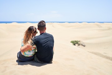 Fototapeta na wymiar Young beautiful couple at sitting backwards and hugging at the beach