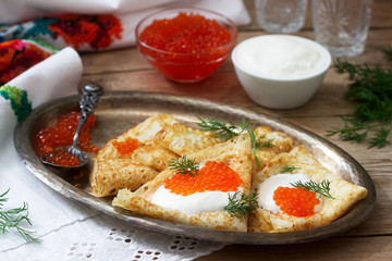 Homemade pancakes with red caviar, sour cream and dill served with vodka. Rustic style.