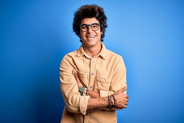 Fototapeta na wymiar Young handsome man wearing casual shirt standing over isolated blue background happy face smiling with crossed arms looking at the camera. Positive person.