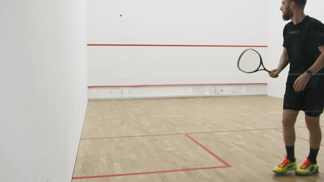 Young athletic man and woman play squash together in the squash court, slow motion