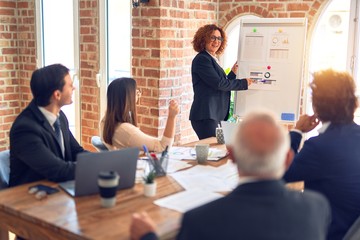 Group of business workers smiling happy and confident in a meeting. Working together looking at presentation using board and charts at the office.