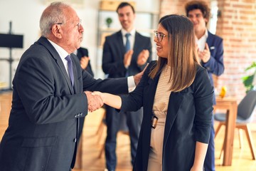 Fototapeta premium Group of business workers smiling happy and confident. Two of them, standing with smile on face shaking hands for agreement. Partners applauding at the office.