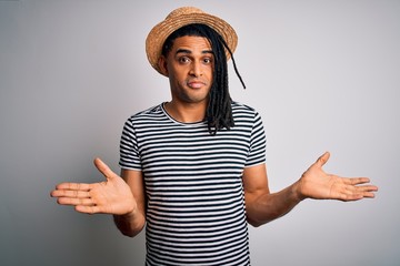 Young african american man with dreadlocks on vacation wearing striped t-shirt and hat clueless and...