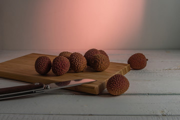 ripe lychee fruits lying on a bamboo board with a knife on a white wooden table