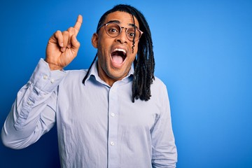 Young handsome african american man with dreadlocks wearing casual shirt and glasses pointing finger up with successful idea. Exited and happy. Number one.