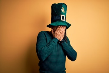 Young african american man wearing green hat with clover celebrating saint patricks day with sad expression covering face with hands while crying. Depression concept.