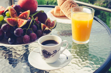 Breakfast table with coffee, orange juice, fruits and croissants