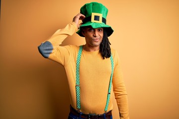 Young african american man wearing green hat celebrating saint patricks day confuse and wonder about question. Uncertain with doubt, thinking with hand on head. Pensive concept.
