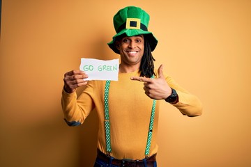 Young african american man wearing green hat holding banner celebrating saint patricks day very happy pointing with hand and finger