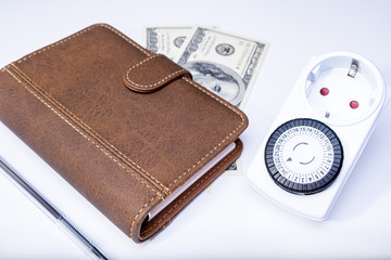24 Hour 7 days a week timer switch for energy and money saving, modern solutions for lower reduce electricity consumption and counting budget - money, notebook, timer and a pen on the table
