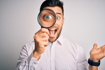 Young detective man looking through magnifying glass over isolated background very happy and excited, winner expression celebrating victory screaming with big smile and raised hands