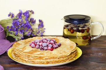 stack of thin pancakes with cranberries, herbal rosehip drink on wooden table for Shrovetide celebration. Russian folk tradition, soft focus