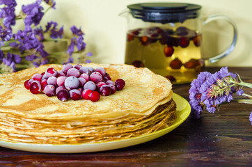 stack of thin pancakes with cranberries, herbal tea from rose hips for a Shrovetide celebration close up. Russian folk tradition, soft focus