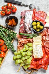 Italian antipasto, wooden cutting board with prosciutto, ham, parma,  goat  and Camembert cheese, olives, grapes. antipasti. Gray background. Top view