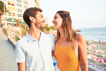 Obraz premium Young beautiful couple on vacation smiling happy and confident. Standing with smile on face hugging at the beach