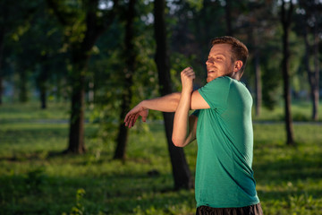 Guy stretching his arms during warming-up for training in nature