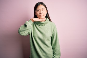 Young beautiful asian woman wearing green winter sweater over pink solated background cutting throat with hand as knife, threaten aggression with furious violence