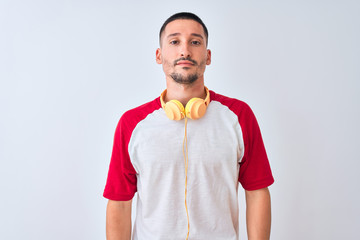 Young handsome man wearing headphones over isolated background with serious expression on face. Simple and natural looking at the camera.