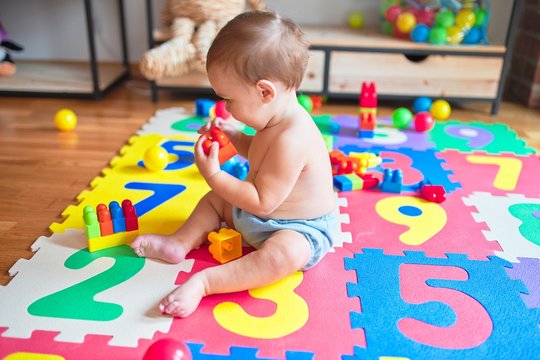 Beautiful toddler sitting on puzzle carpet playing with building blocks at kindergarten