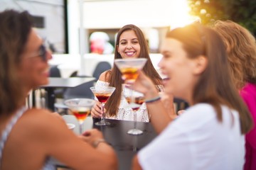 Beautiful group of women sitting at terrace of restaurant drinking cocktails speaking and smiling
