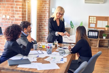 Group of business workers smiling happy and confident. Working together with smile on face. Middle age beautiful woman standing explaining documents at the office