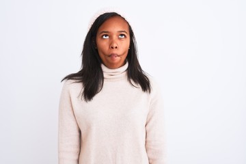 Beautiful young african american woman wearing turtleneck sweater and winter hat making fish face with lips, crazy and comical gesture. Funny expression.