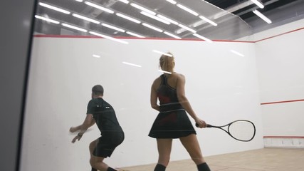 Young athletic man and woman play squash together in the squash court, slow motion, camera is behind the glass