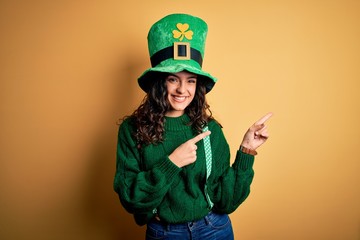 Beautiful curly hair woman wearing green hat with clover celebrating saint patricks day smiling and looking at the camera pointing with two hands and fingers to the side.