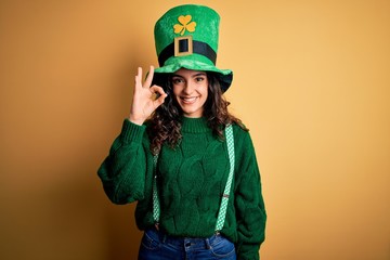 Beautiful curly hair woman wearing green hat with clover celebrating saint patricks day smiling positive doing ok sign with hand and fingers. Successful expression.