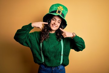 Beautiful curly hair woman wearing green hat with clover celebrating saint patricks day smiling...