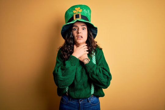 Beautiful curly hair woman wearing green hat with clover celebrating saint patricks day shouting and suffocate because painful strangle. Health problem. Asphyxiate and suicide concept.