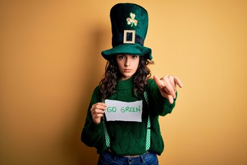 Beautiful curly hair woman wearing hat with clover holding banner with go green message pointing...