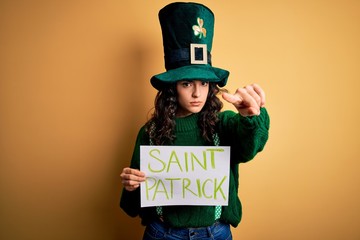 Beautiful curly hair woman wearing green hat holding banner with saint patricks message pointing...