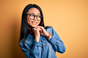 Young beautiful chinese woman wearing casual denim shirt over isolated yellow background laughing...