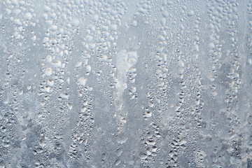 Frozen drops of condensed steam water drops on the transparent window glass. Clean background. Condensation of moisture at extreme temperatures. Water vapor condenses on cold window glass and freezes