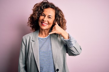 Middle age beautiful businesswoman wearing elegant jacket over isolated pink background smiling doing phone gesture with hand and fingers like talking on the telephone. Communicating concepts.