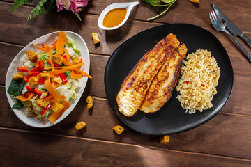 Pescado a la plancha con especias y ensalada de lechuga zanahoria y aderezo mil islas y limon arroz en mesa de madera