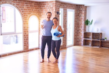 Middle age beautiful sporty couple smiling happy. Standing with smile on face hugging and holding mat at gym