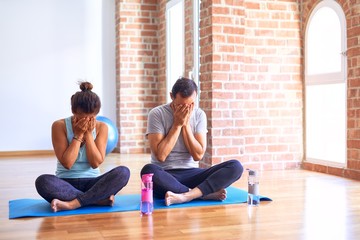 Middle age sporty couple sitting on mat doing stretching yoga exercise at gym with sad expression covering face with hands while crying. Depression concept.