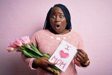 Plus size african american woman holding love mom message and tulips on mothers day scared in shock...