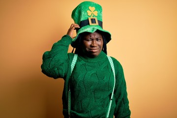 Fototapeta premium Plus size african american woman with braids wearing green hat with clover on st patricks day confuse and wonder about question. Uncertain with doubt, thinking with hand on head. Pensive concept.