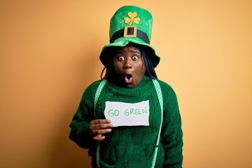 Plus size african american woman wearing green hat holding paper on saint patricks day scared in...