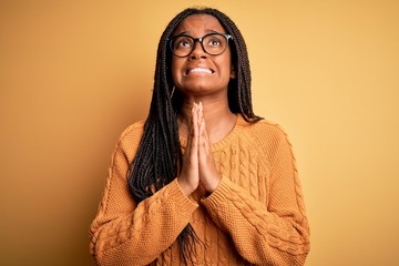 Young african american smart woman wearing glasses and casual sweater over yellow background...