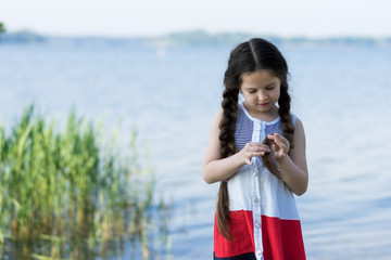 Portrait of a beautiful little girl with long hair near the lake on a sunny day.